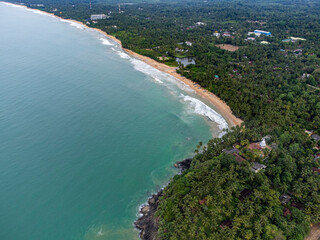 Sri Lanka. Ahungalla beach: ocean, coastal waves, sand. Tropical trees and palm trees grow along the beach line. Top view, shooting from a drone.