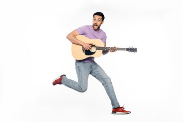 Fototapeta na wymiar amazed man in jeans and purple t-shirt levitating while playing acoustic guitar on white.