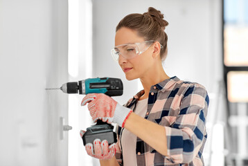 repair, construction and building concept - woman or builder with perforator drilling wall at home
