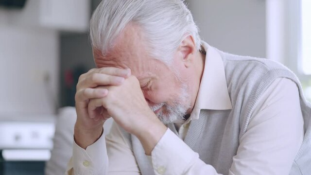 Unhappy senior man sitting in room alone, crying upset with problem, loneliness