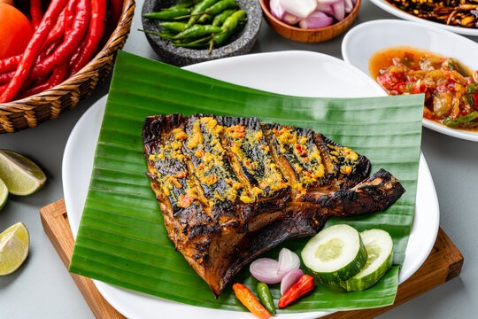 Ikan Pari Bakar or Grilled Sting Ray in chilli curry sauce served on banana leaf with shallots cucumber and chili.