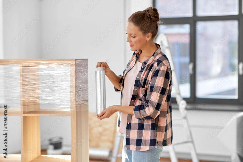 Sticker repair, people and real estate concept - smiling happy woman packing shelf with plastic wrap and moving to new home