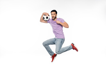 happy man in jeans and purple t-shirt levitating while pointing at football on white.