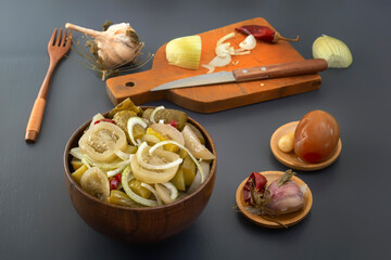 Fermented green tomatoes and cucumbers with onions and pickled garlic next to a cutting board with...