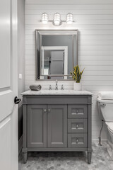 A remodeled half bath with a grey vanity and marble top with a chrome faucet. Shiplap is on the back wall with beautiful octagon tiles on the floor.