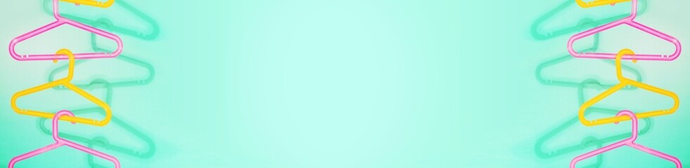 Sale banner with colored plastic hangers hung on top of each other on a mint background with shadows and copy space. The concept of summer sale and selling children's clothing