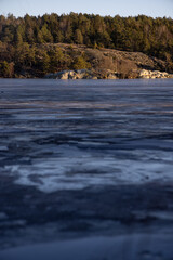 Beautiful natural Scandinavian landscape. Frozen lake with forest and stones at the shore line. Sunny late autumn or winter day in the nature in Sweden. Real is beautiful