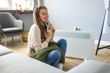 Young woman in sweater feeling cold, waiting for the house to heat up, controlling heating system...