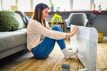Young Woman With sweater Suffering From Cold Sitting Near Heating Radiator At Home. Energy Saving...