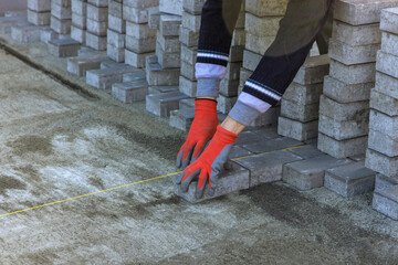 The master in gloves lays paving stones in layers pathway paving by professional paver worker.