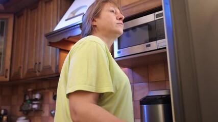 Eating disorder, middle-aged woman opens refrigerator at night and drinks milk from a plastic bottle.