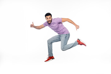 Fototapeta na wymiar amazed man in jeans and purple t-shirt levitating while showing thumbs up isolated on white.
