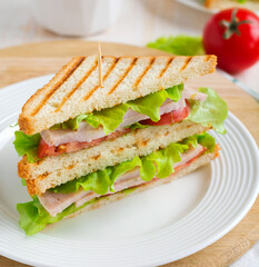 Sandwich for breakfast with stuffed tomatoes with ham and lettuce on a light wooden background. Selective focus.