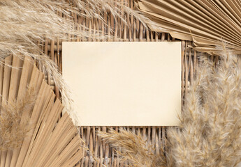 Boho scene with blank card on a wattled table near dry palm leaves and pampas grass