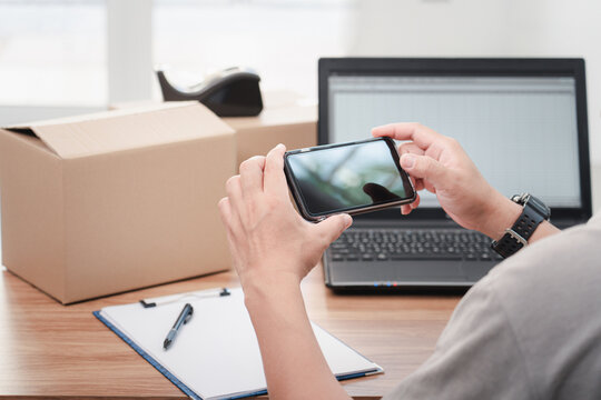 Close up hand a man use smartphone take photo parcel box  to store information and use laptop to register in the online system