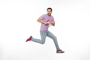 happy man in jeans and purple t-shirt levitating while holding megaphone on white.