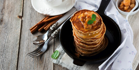 Stack of pancakes from buckwheat flour with baked apples and cinnamon on old wooden background. A healthy breakfast. Selective focus.
