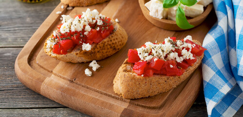Fototapeta premium Bruschetta with tomatoes, feta cheese and basil. Traditional Greek snack on wooden background. Selective focus.