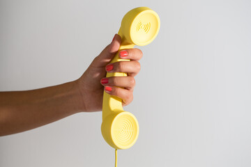 hand of a woman with red nails holding a yellow retro old-fashioned phone handset on white background 