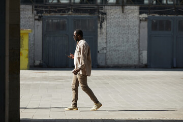 Wide angle shot of adult African-American man walking in urban city street, copy space