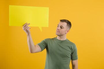 Happy guy smiling and holding blank speech balloon near head against yellow background