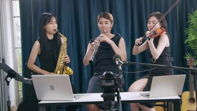 Beautiful Female musician playing instrumental oboe saxophone violin flute guitar use laptop computer singing online streaming broadcast teaching tutorial webcam live show
