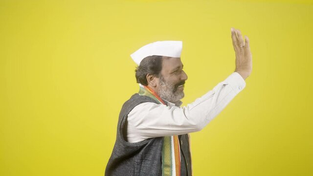 Senior Indan Politician greeting by waving hand on yellow studio background - concept of Politics, lawmaker and poll campaign.