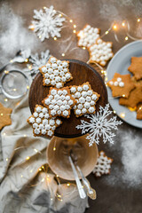 Snowflake cookies in sugar glaze on a wooden stand on a table with a garland and utensils. New Year's pastries.