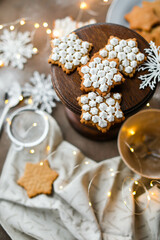 Snowflake cookies in sugar glaze on a wooden stand on a table with a garland and utensils. New Year's pastries.