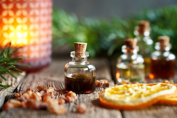 A bottle of myrrh essential oil with myrrh resin, orange and fir in the background - obrazy, fototapety, plakaty