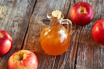 A jug of apple cider vinegar with fresh red apples