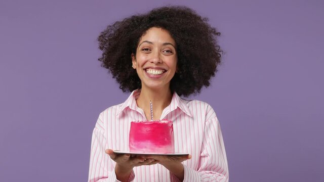 Excited Fun Blithesome Charismatic Charming Young Black Woman 20s Years Old Wears Pink Shirt Hold In Hand Birthday Cake Blow Out Candle Isolated On Plain Pastel Light Purple Background Studio Portrait