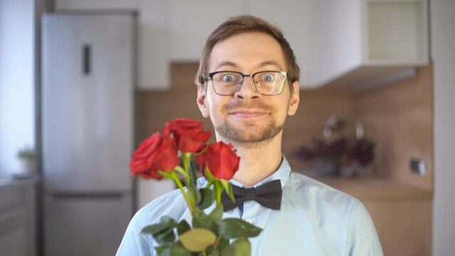 Passionate young male nerd in glasses and elegant outfit with bow tie holding red rose and looking at camera. Valentine's day concept.