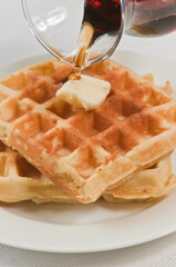 top view, close up of two freshly prepared waffles with a pat of butter and maple syrup pouring over the top