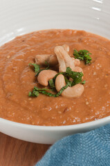 top view, close up of Eggplant and Tomato Soup with cashew nuts ripe basil in a round, white, ceramic bowl