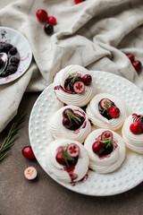 Mini meringue with cranberry jam, fresh cranberries and rosemary on a beige table with a tablecloth and berries.