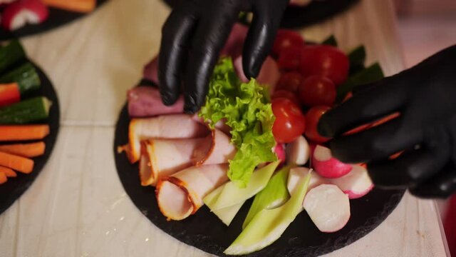 Close up hands of cook serving meat appetizer with vegetables and lettuce salad for dinner. Slices meat, ham, sausage, tomatoes, salad and vegetable for snack on festive table