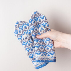 Woman holds knitted mittens on white background. Warm handmade mittens for winter. Square. White and blue pattern