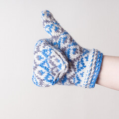 Woman in knitted mittens on white background. Warm handmade mittens for winter. Square. White and blue pattern. Thumbs up