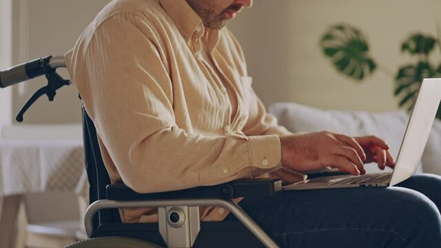 Busy young man sitting in wheelchair, working on laptop, distance education