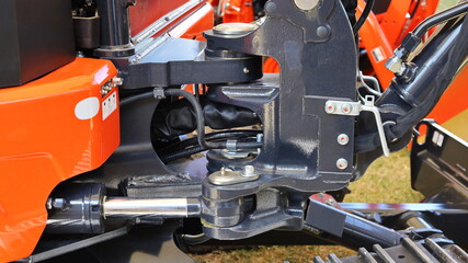 New excavator pivot joints. Coupling with hydraulic pipe axis of a small orange backhoe. Closeup and focus on the subject.