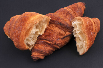 Croissants au beurre dont un coupé en deux en gros plan sur fond noir