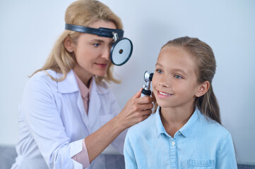 Woman examining girls ear through frontal reflector