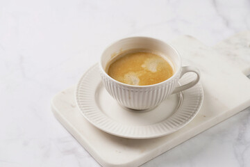 a white porcelain cup with coffee with milk on a marble board on a white table
