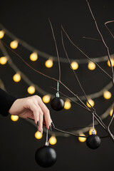 Female hand hanging baubles on branches to decorate house with black decorations