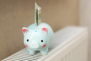 Pig piggy bank and dollar bills on a radiator indoors close-up. Heating concept.