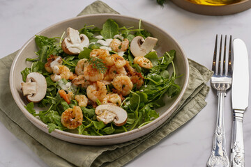 Arugula salad with shrimp and champignons, olive oil and dill on a wooden board on a white surface