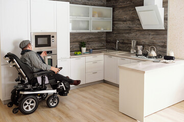 Middle aged man with disability sitting by electric oven in large comfortable kitchen in home...