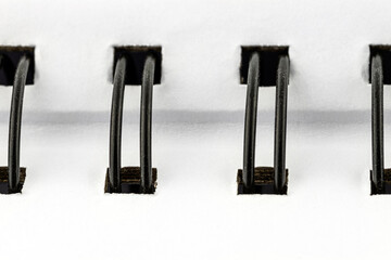 Macro photo of a white notebook with a black metal spiral connecting the pages.