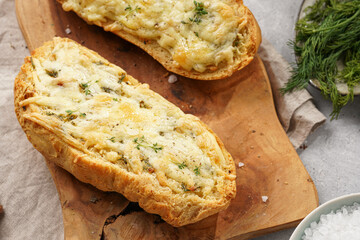 Two halves of garlic and butter bread - baguette on a wooden board, sea salt, pepper, dill and garlic cloves on a grey concrete background, top view
